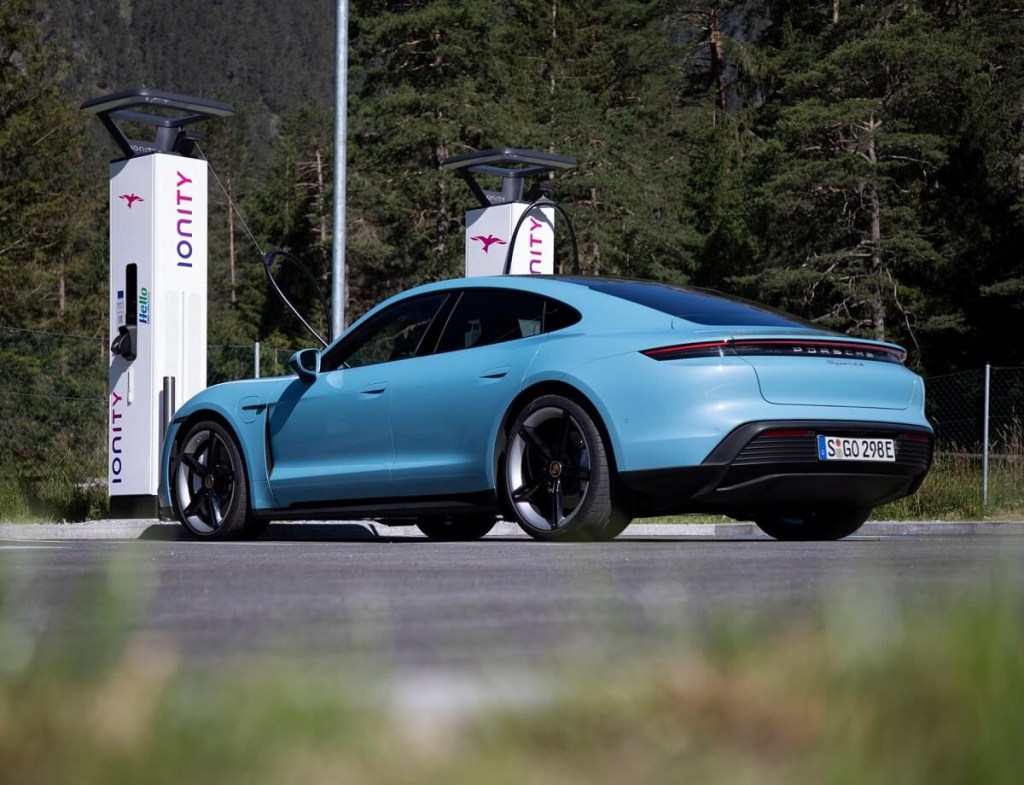 A light blue Porsche Taycan parks by electric car chargers.