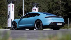 A light blue Porsche Taycan parks by electric car chargers.