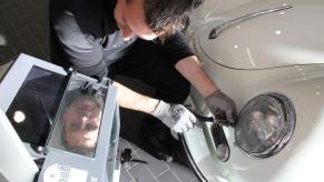 A mechanic performing maintenance on a set of headlights at a Porsche shop in Stuttgart, Germany