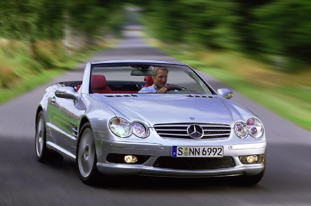 A used 2003 Mercedes-Benz SL500 or SL55 luxury sports car corners with it's folding roof down. 