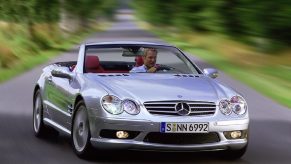 A used 2003 Mercedes-Benz SL500 or SL55 luxury sports car corners with it's folding roof down.