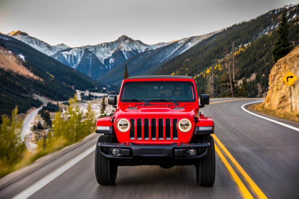 A head on view of a red Jeep Wrangler driving down a road with a mountain scenery in the background.