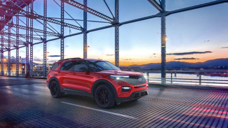 A red Ford Explorer crosses a bridge at sunset.