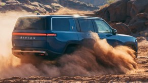 A blue 2023 Rivian R1S full-size luxury electric SUV is driving through the sand.