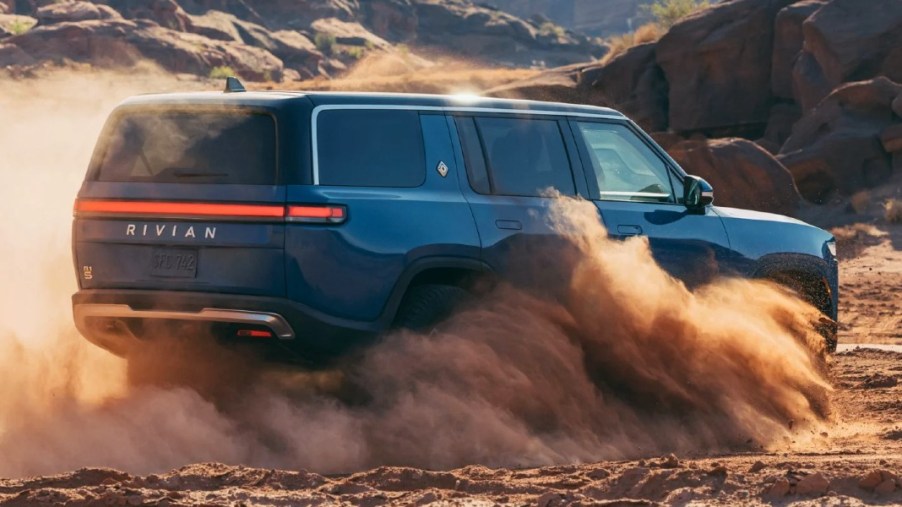 A blue 2023 Rivian R1S full-size luxury electric SUV is driving through the sand.