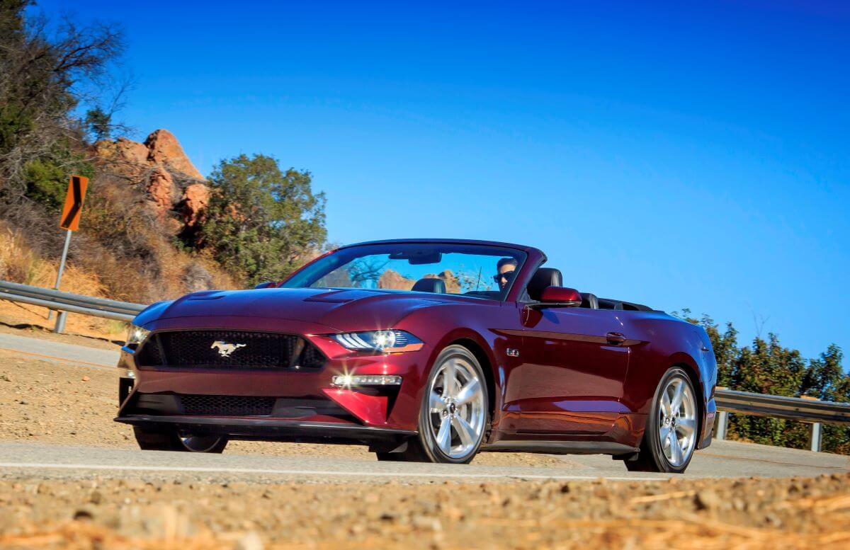 A Royal Crimson 2018 Ford Mustang Convertible coupe model driving on a twisting country road