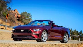 A Royal Crimson 2018 Ford Mustang Convertible coupe model driving on a twisting country road