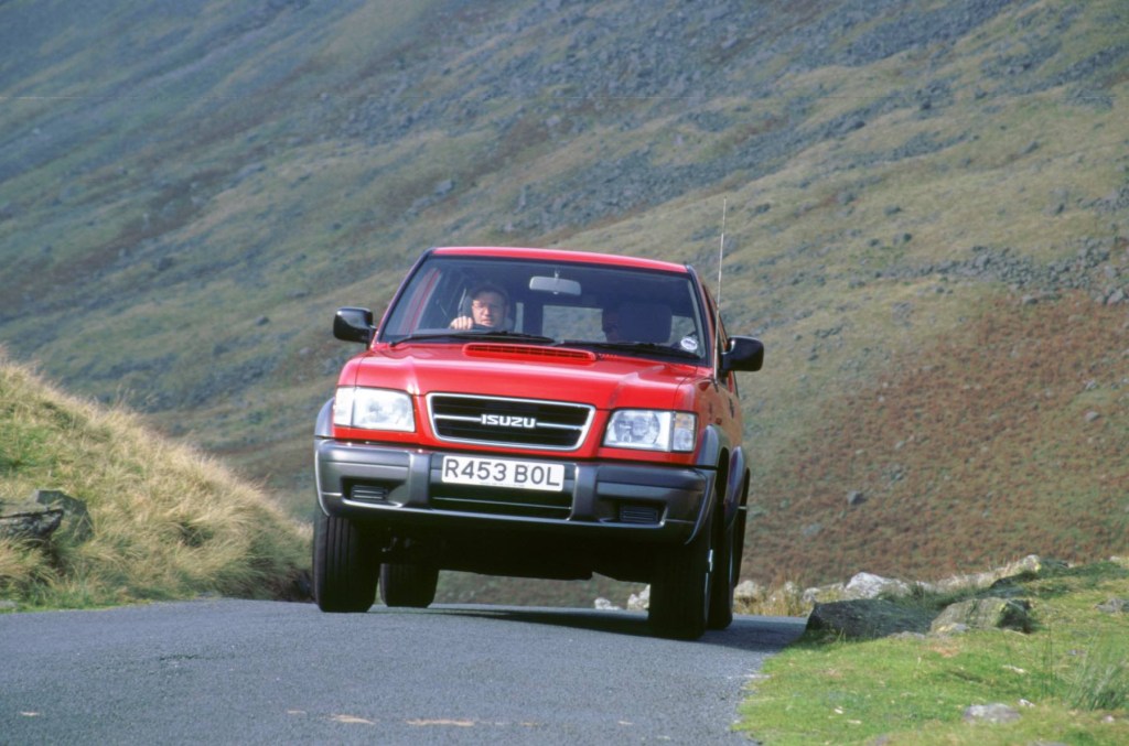 A red second-generation Isuzu Trooper drives on a mountain road.