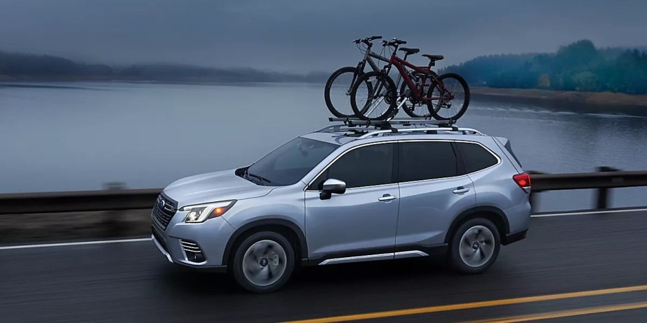 A blue 2023 Subaru Forester small SUV is driving on the road. 