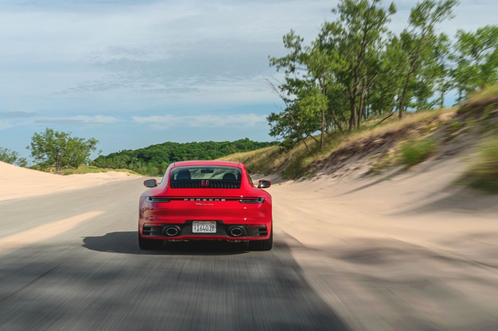 A red Porsche 911 Carrera drives away alongo a sandy beach road. 