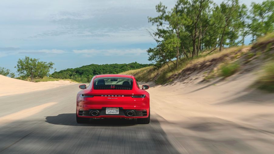 A red Porsche 911 Carrera drives away alongo a sandy beach road.