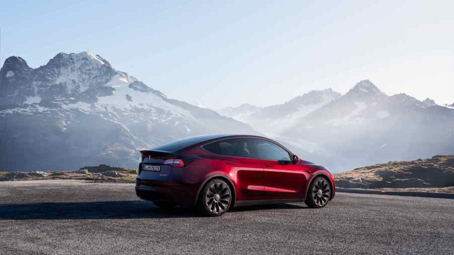 A red Tesla Model Y with mountains in the background.