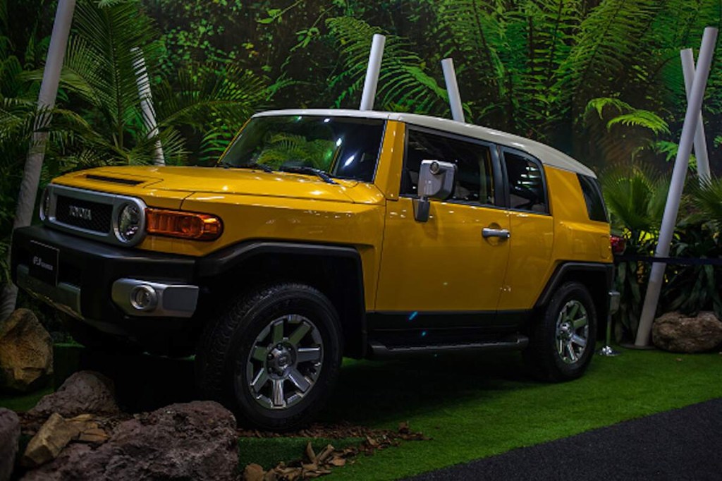 A yellow Toyota FJ Cruiser parked on a platform in front of a manufactured forest scene. 