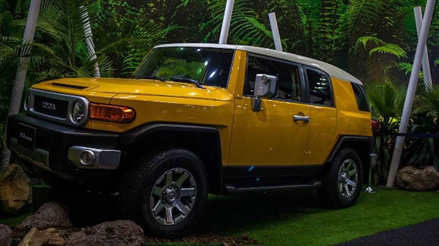 A yellow Toyota FJ Cruiser parked on a platform in front of a manufactured forest scene.
