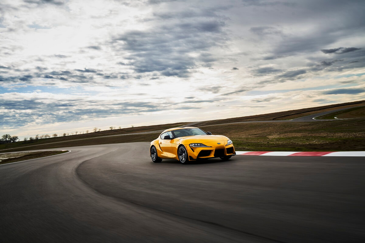 A bright yellow Toyota GR Supra 2.0 takes a corner on a track.