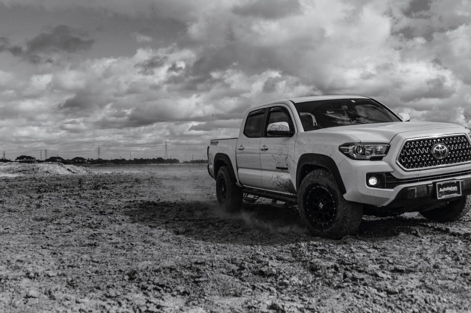 Toyota Tacoma pickup truck driving across a muddy field in a black and white photo, clouds visible in the background.