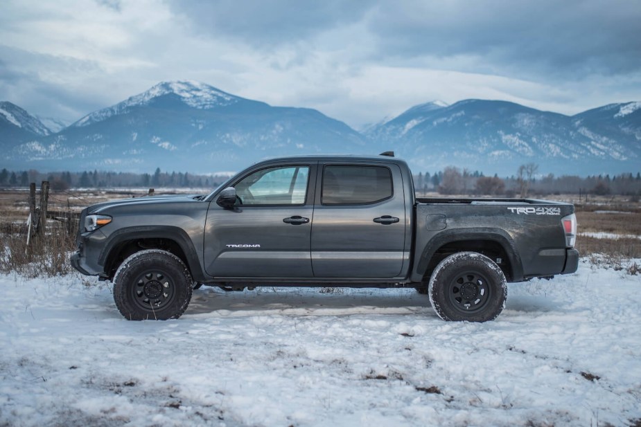 A gray four-door Toyota Tacoma pickup truck parked in front of mountains, in a snowy field.