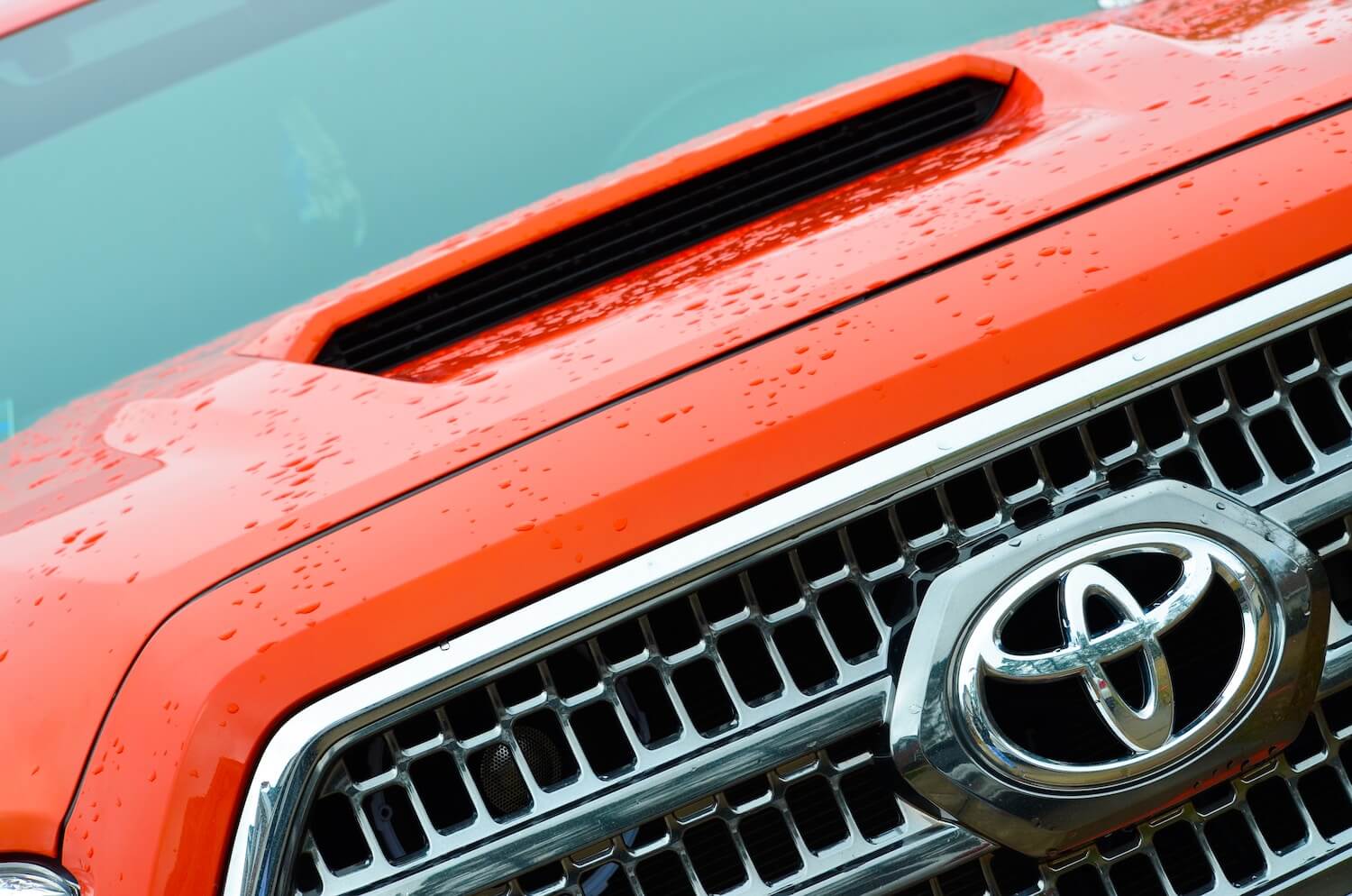 Closeup of the Toyota logo in the grille of an orange Tacoma pickup truck.
