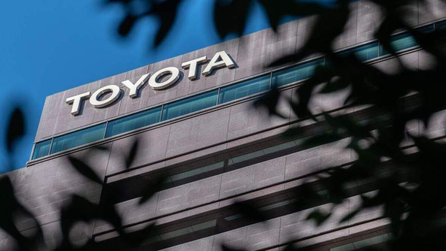 A Toyota logo seen through trees on a building in front of blue skies.