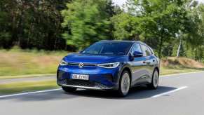 A blue Volkswagen ID.4 EV drives along a road with green trees passing by. The ID.4 was identified in a new recall.