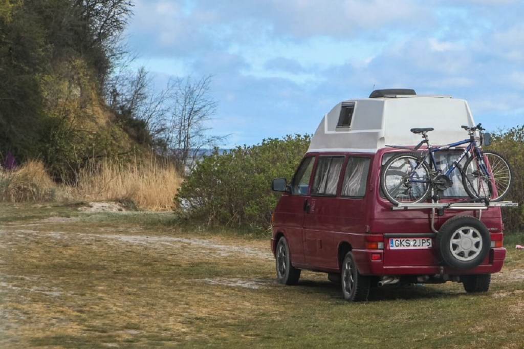 A maroon Volkswagen van parks in a camper site as travel junkies enjoy van life. 