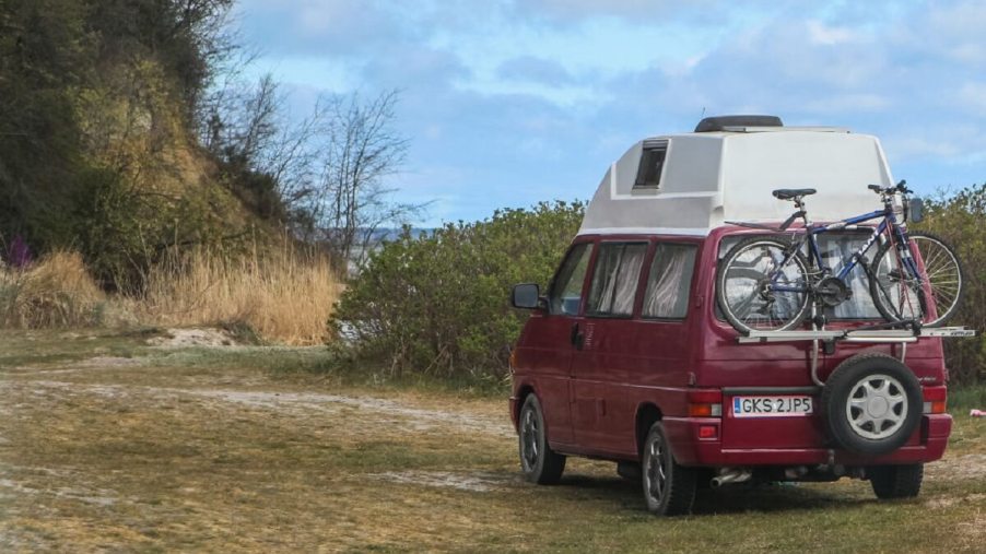 A maroon Volkswagen van parks in a camper site as travel junkies enjoy van life.