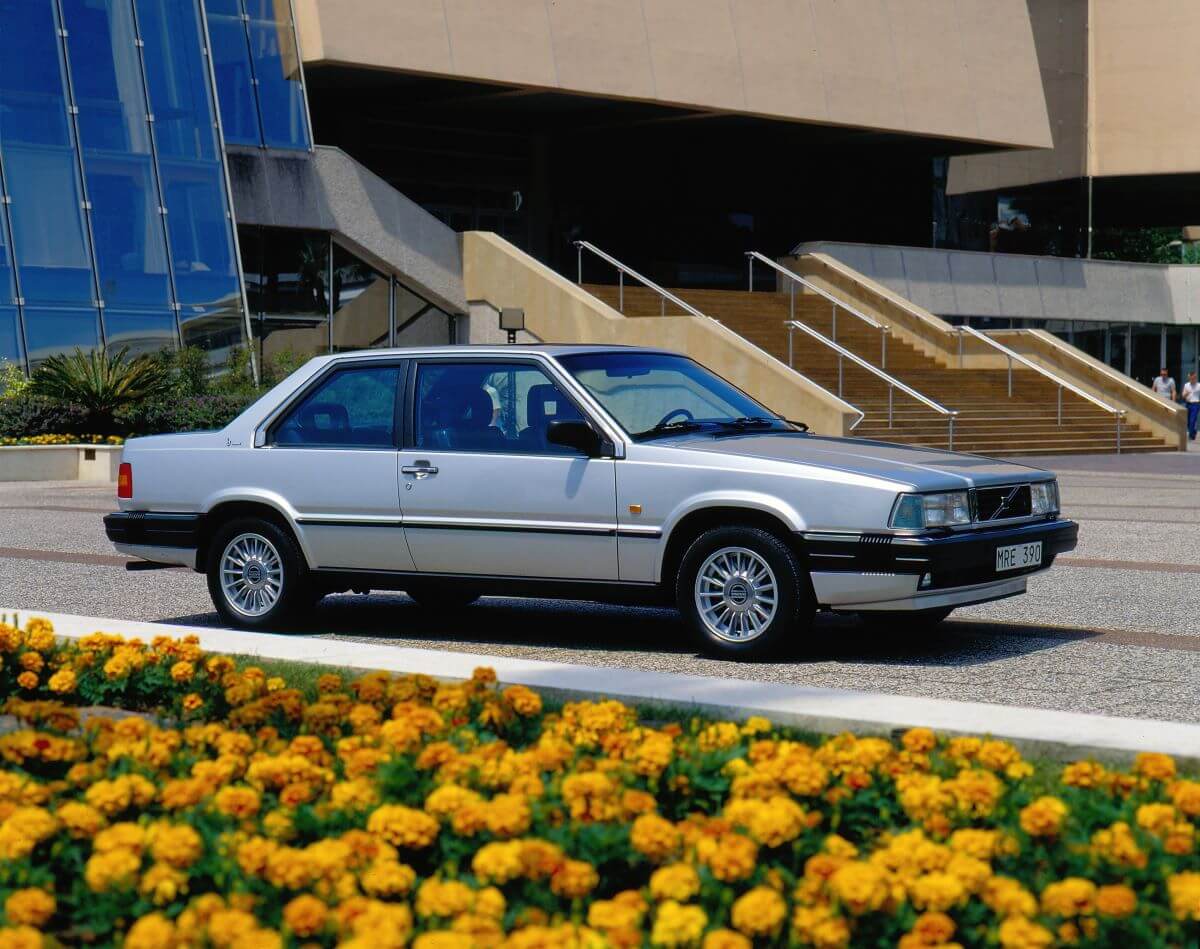 A 1985 Volvo 780 executive car model from the 700 Series parked in front of a row of yellow flowers