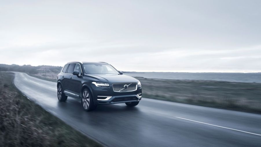 A 2023 Volvo XC90 Recharge AWD in Denim Blue driving down a seaside highway surrounded by clouds and fog