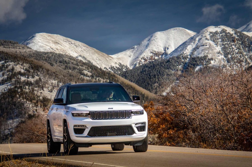 A white 2023 Jeep Grand Cherokee drives in front of a mountain range.