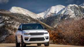 A white 2023 Jeep Grand Cherokee drives in front of a mountain range.
