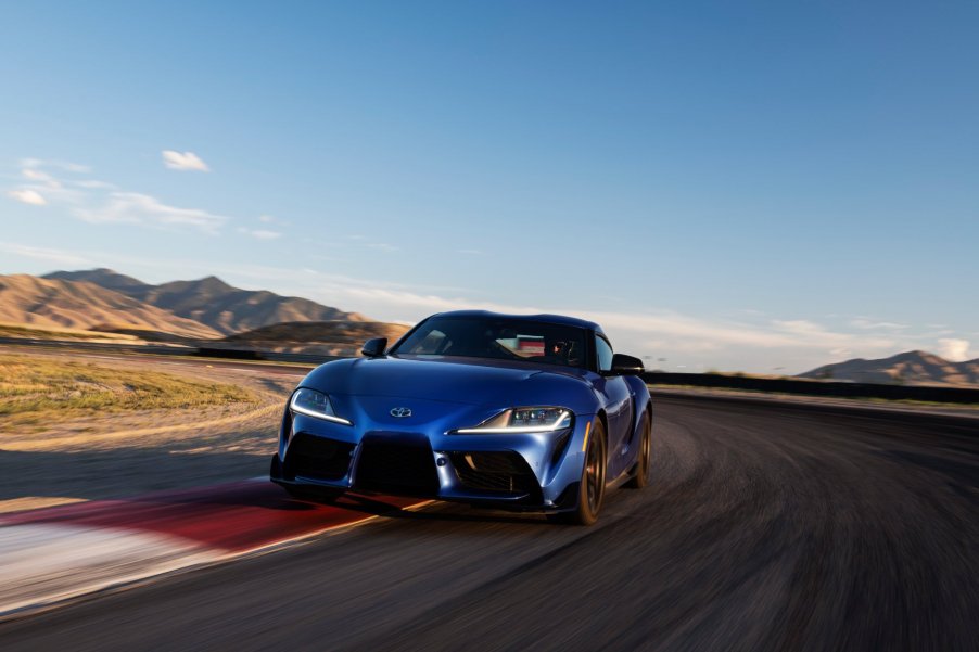 A blue 2023 Toyota Supra drives around a track at sunset with its inline-6 engine under the hood.