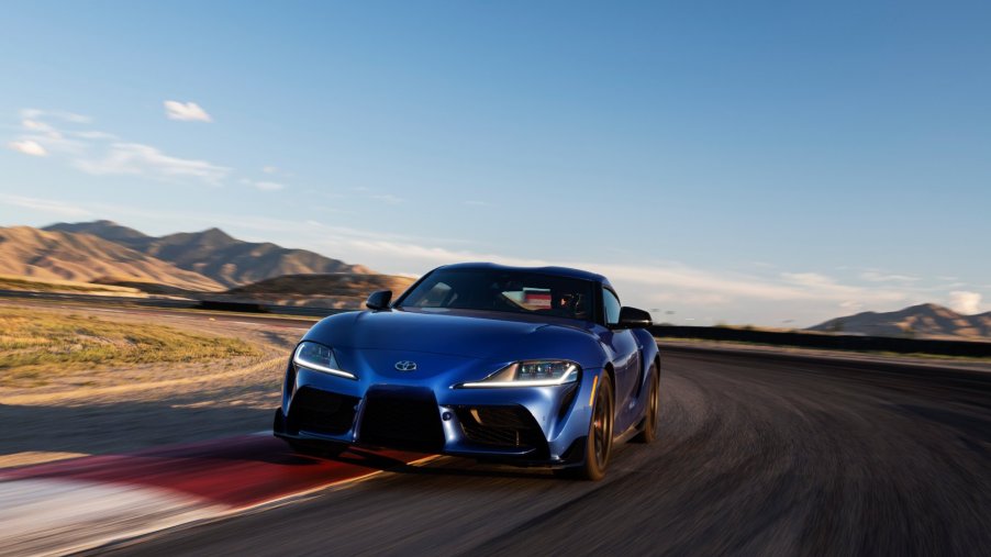 A blue 2023 Toyota Supra drives around a track at sunset with its inline-6 engine under the hood.