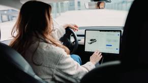 A woman types on the touchscreen of her Tesla vehicle, in front of the cabin camera.