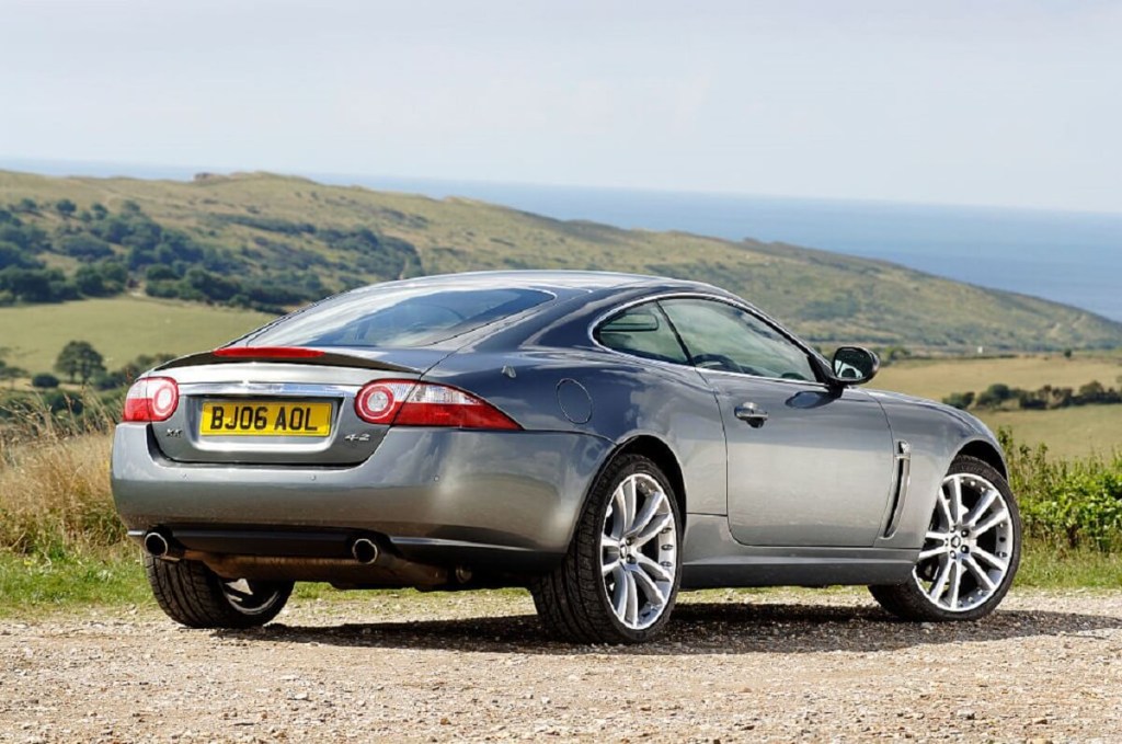 A silver 2007 Jaguar XK luxury sports car parks on a gravel spot in England.