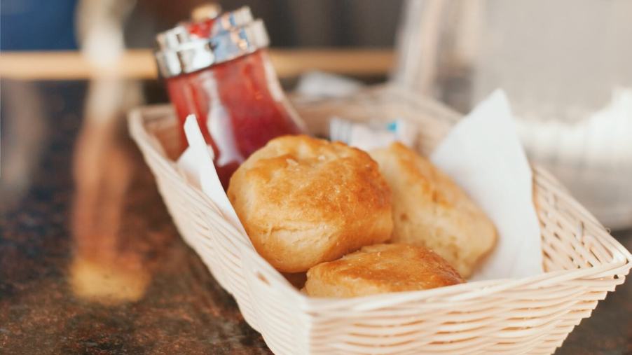 Three biscuits in a basket on a table, jam visible in the background.