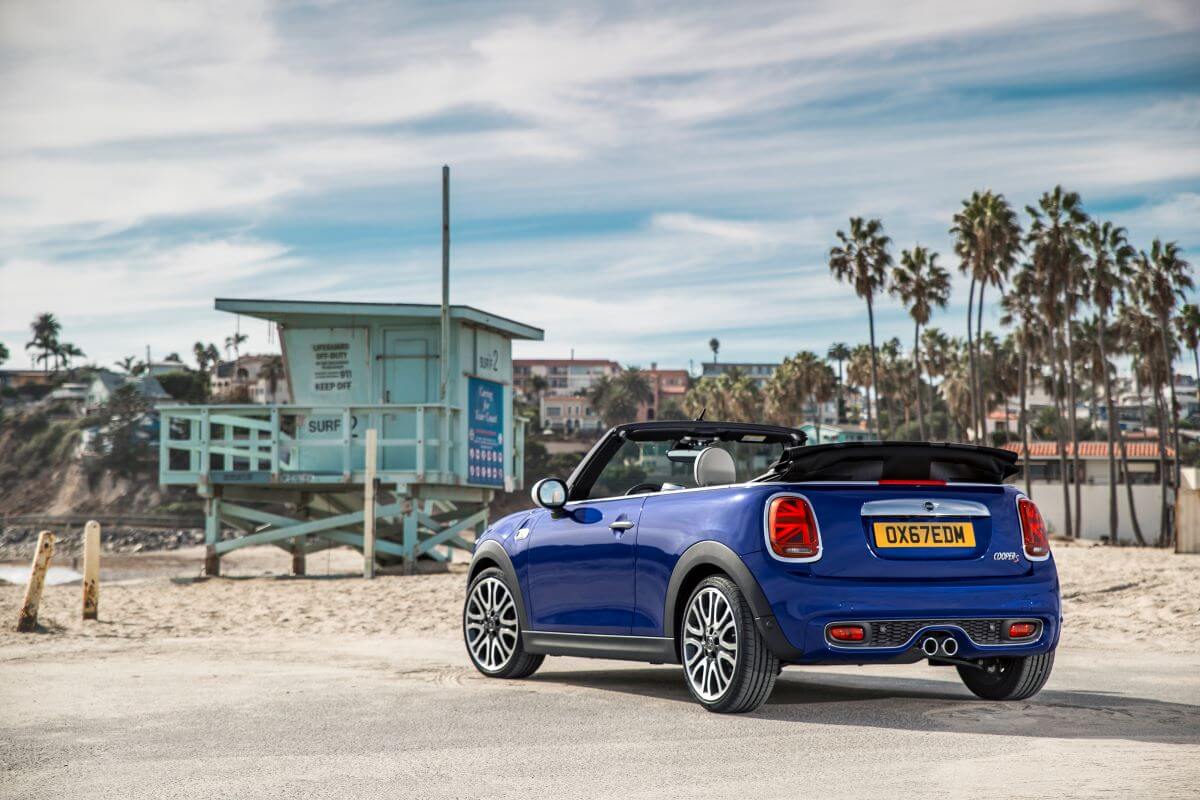 A rear shot of a blue 2019 Mini Convertible compact car model parked on a beach asphalt lot