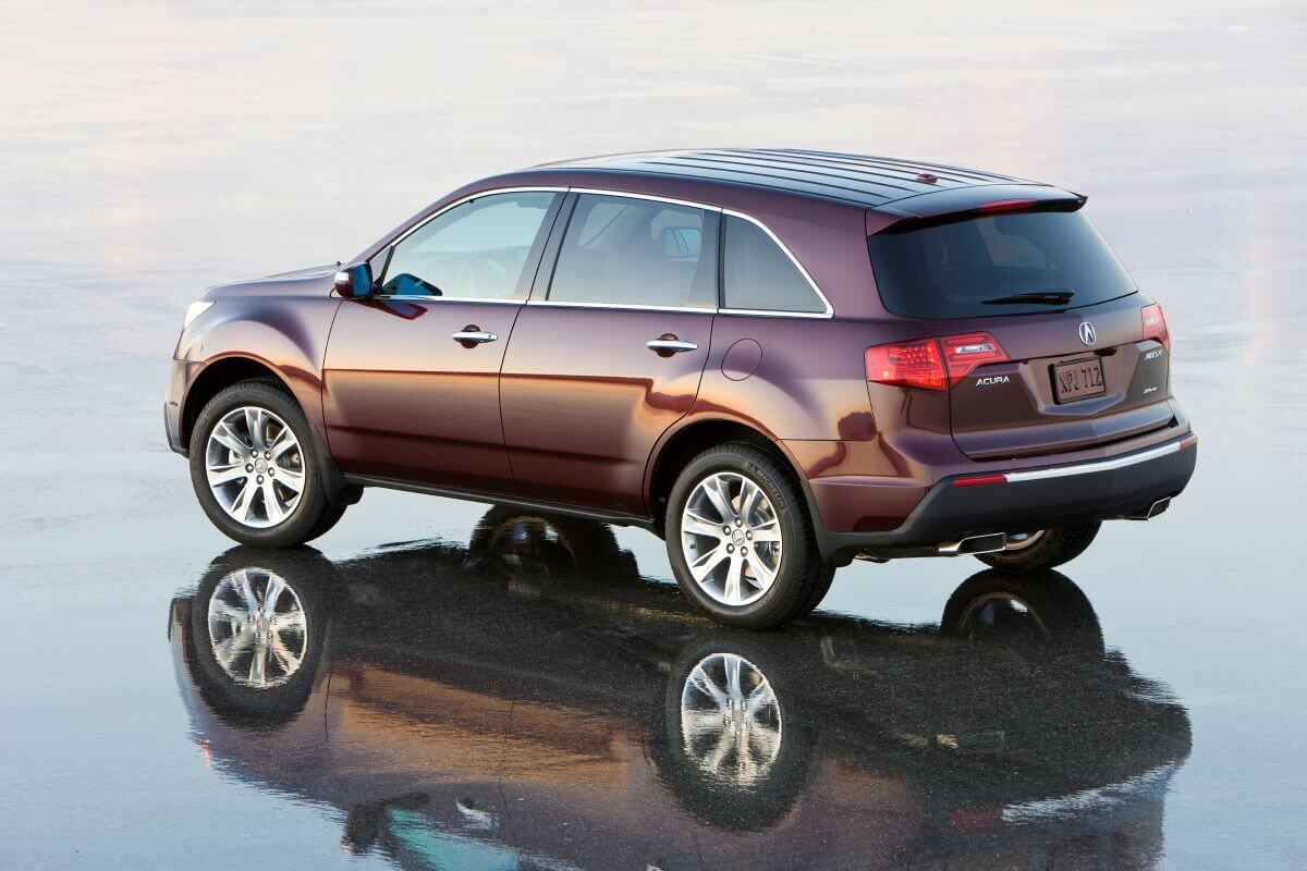 An overhead side profile shot of a red-brown 2010 Acura MDX midsize luxury SUV model on reflective pavement