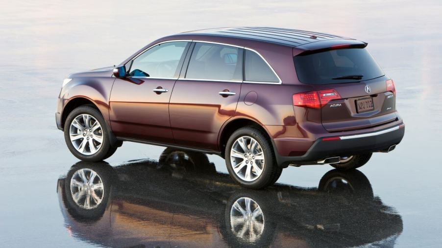 An overhead side profile shot of a red-brown 2010 Acura MDX midsize luxury SUV model on reflective pavement