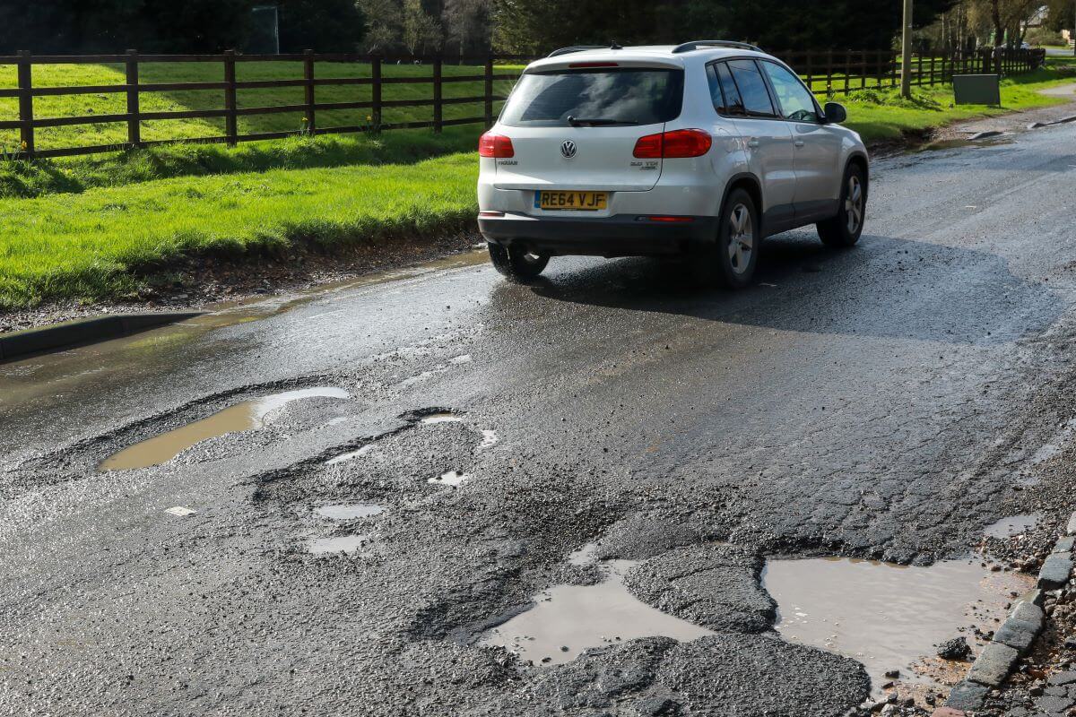 A white Volkswagen model driving on a South Bucks district road in Slough covered in large potholes