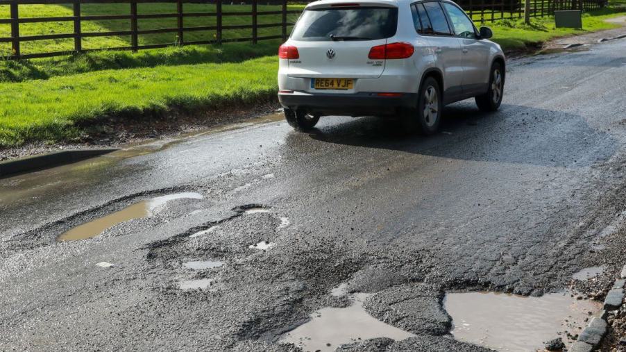 A white Volkswagen model driving on a South Bucks district road in Slough covered in large potholes