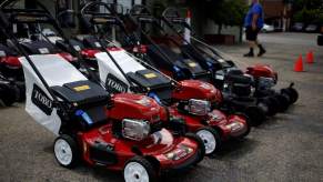 A row of lawn mowers, that may help with the consideration of electric vs. gas lawn mowers, all lined up outside of building.