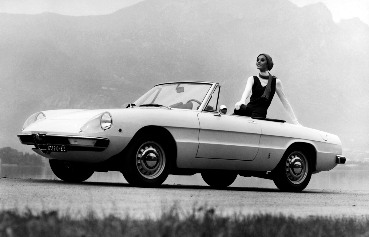 A black and white image of a model in a 1969 Fiat Duetto Spider.