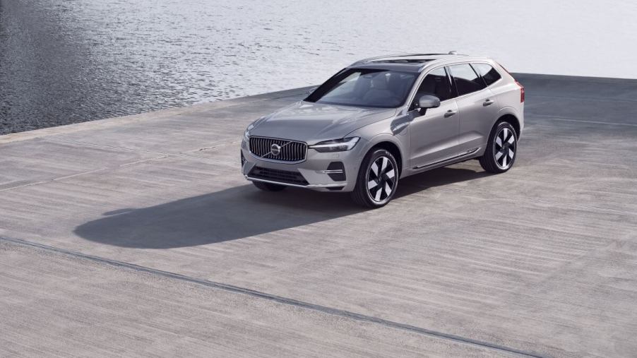 A silver-gray 2023 Volvo XC60 compact luxury SUV model parked on a concrete dock near the water.