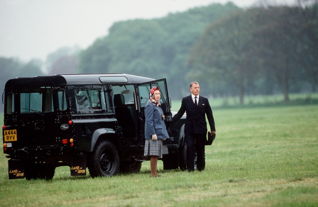 The queen and her black Land Rover Defender in a green field