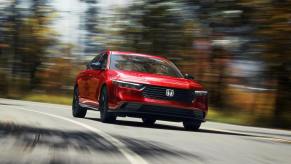 A red 2023 Honda Accord Sport-L midsize sedan model driving past autumn trees as the background blurs