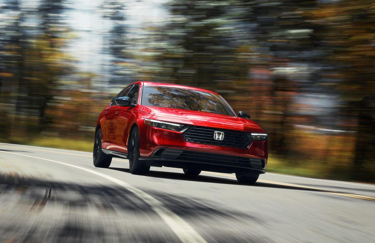 A red 2023 Honda Accord Sport-L midsize sedan model driving past autumn trees as the background blurs