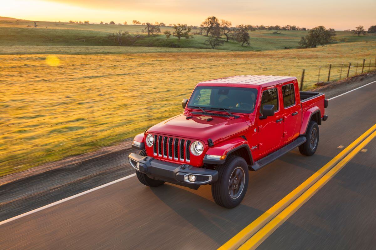 A red 2023 Jeep Gladiator Overland midsize pickup truck model driving past empty farm fields on a highway