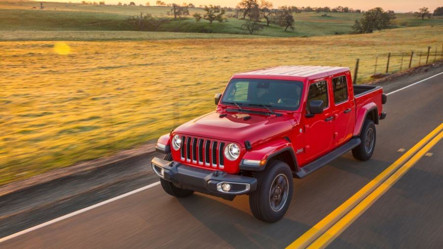 A red 2023 Jeep Gladiator Overland midsize pickup truck model driving past empty farm fields on a highway