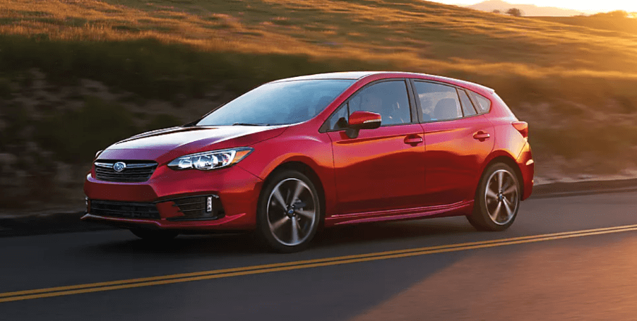 A red 2023 Subaru Impreza Hatchback model driving on a country highway as the sun sets behind it