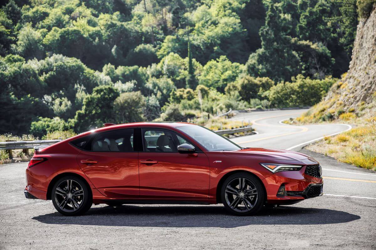 A side profile shot of a red 2023 Acura Integra A-Spec luxury liftback sedan model parked near a twisting road